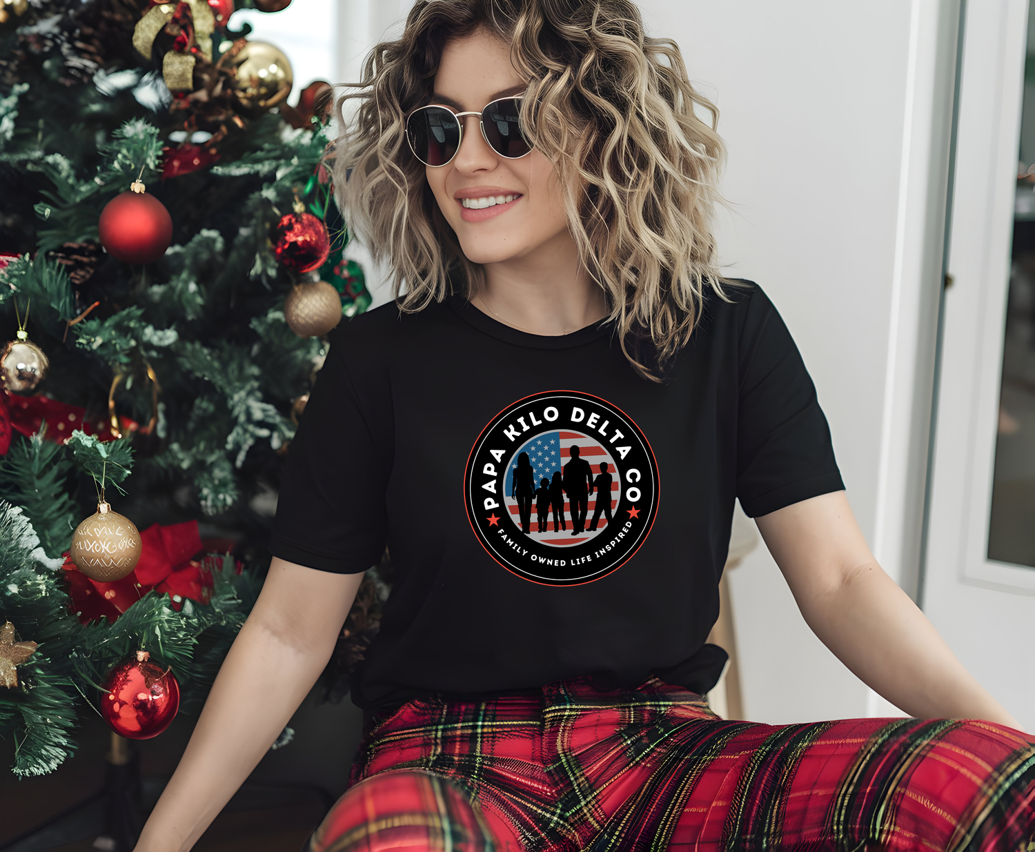 picture of a women in front of a decorated christmas tree wearing a t-shirt with the papa kilo delta logo